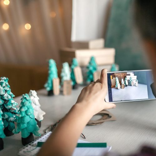 Cute girl prepared DIY gifts and making photo to share with friends and relatives, a green cone as if it is small toy pine tree, tags and festive boxes, handmade presents, zero waste holidays